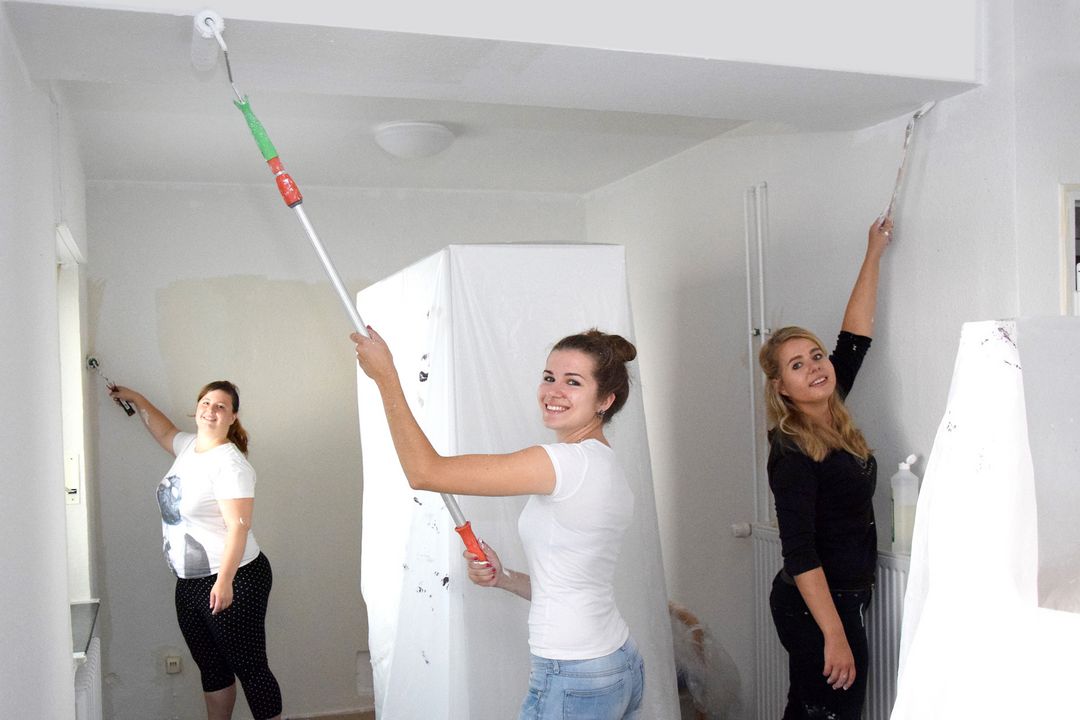 Drei Frauen streichen die Wände eines Zimmers mit weißer Farbe.