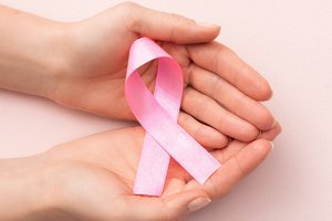 Zwei Hände halten eine rosa Schleife